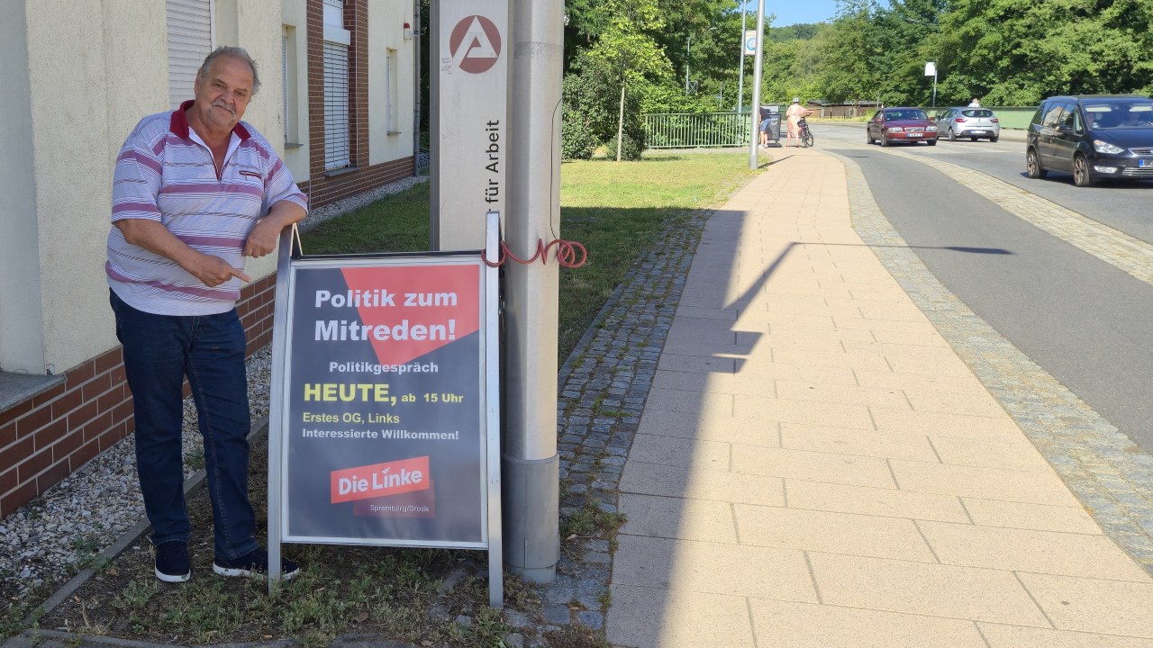 Fingerzeig auf das Einladungsplakat für die Veranstaltung "Politik zum Mitreden!", der Spremberger Linken